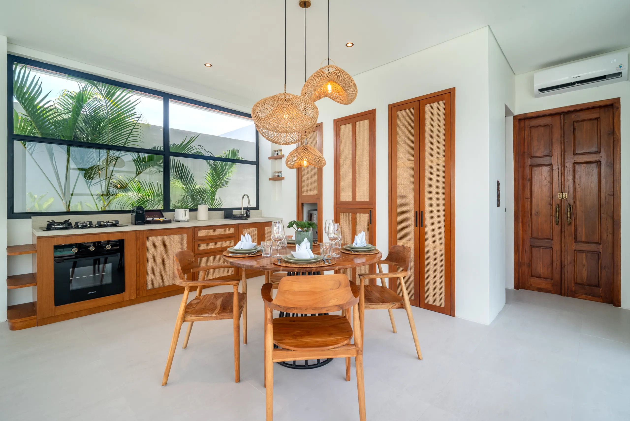 Open kitchen and dining area with teak joinery and rattan pendant lights at Villa Sofra